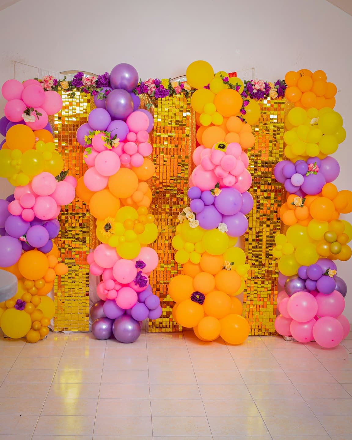 Colonne di palloncini colorati davanti a un muro di paillettes dorate.